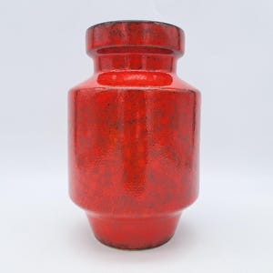 Puede incluir: Un jarrón de cerámica rojo con un esmalte moteado. El jarrón tiene un cuerpo redondeado y una abertura ligeramente acampanada.