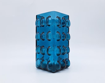 May include: A square, teal-colored glass vase with a unique bubble design. The vase has a geometric shape with rounded, protruding bubbles arranged in vertical rows. The glass is transparent, allowing light to pass through, and is set against a white background.