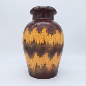 Peut inclure: Un vase en céramique marron avec un corps arrondi et un dessus marron foncé. Le vase présente un motif répétitif de lignes irrégulières orange et marron sur sa circonférence. C'est un objet décoratif.