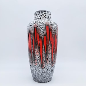 Peut inclure: Un vase en céramique de grande taille, orné d'un motif noir et blanc moucheté. Des coulures verticales rouges et noires décorent le corps du vase. De forme cylindrique, il mesure environ 30 cm de haut, idéal pour la décoration intérieure.