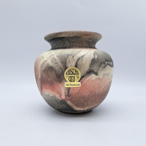 Könnte beinhalten: Eine kleine, runde Keramikvase mit breitem Körper und schmalem Hals. Die Vase hat eine Mischung aus Farben, darunter Brauntöne, Grau und Rosa. Die Vase hat einen Aufkleber mit der Aufschrift "RUSCHA art echt Handarbeit".