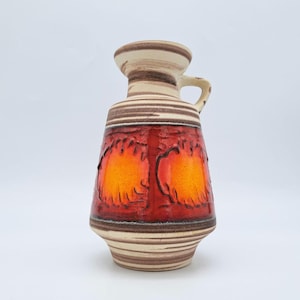 May include: A vintage ceramic vase with a handle, featuring a striking design. The vase has a cream-colored top and base with brown horizontal stripes. The central section showcases a vibrant orange and red pattern, possibly depicting stylized trees.