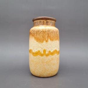 Puede incluir: Un jarrón de cerámica cilíndrico con superficie texturizada. El jarrón presenta un degradado de colores, desde un borde marrón oscuro hasta una base amarillo claro, con una banda amarilla en el medio. Adecuado para la decoración del hogar.