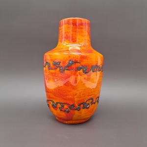 Może przedstawiać: Pomarańczowy i czarny ceramiczny wazon z falistym wzorem. Wazon ma błyszczące wykończenie i zaokrąglony kształt.
