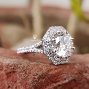 Puede incluir: Un anillo de plata con un gran diamante de forma octogonal rodeado por un doble halo de diamantes más pequeños. El anillo tiene una banda dividida.