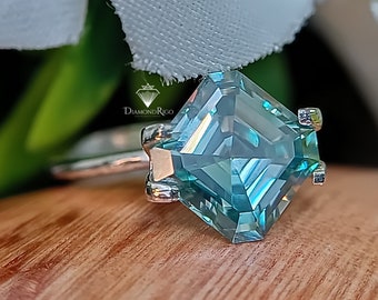 May include: A silver ring with a large, square-shaped, blue moissanite gemstone. The gemstone has a faceted cut and is set in a simple, four-prong setting.