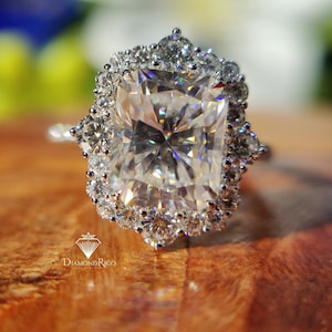 Op de afbeelding: Een zilveren ring met een grote, vierkante diamant omringd door een halo van kleinere diamanten.