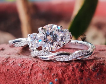 May include: A silver engagement ring set with a large round center stone and two smaller round stones on either side. The band is twisted and has small diamonds set into it.