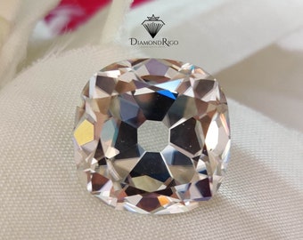 May include: A clear, faceted, square-shaped gemstone with a hole in the center. The gemstone is on a white fabric background.