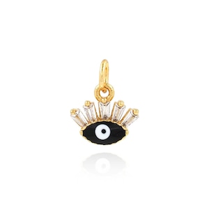 May include: Gold charm with a black evil eye with a white pupil surrounded by clear baguette-shaped crystals.