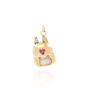May include: Gold backpack charm with a white enamel body and red gemstone accents. The charm has a small diamond detail on the straps.
