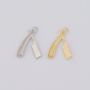 May include: Two small, detailed razor charms. One is silver-colored, the other is gold-colored. Both have a textured handle and a blade. The charms are designed for jewelry making or crafting projects.