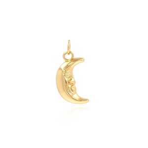 Puede incluir: Un amuleto de luna creciente de oro con una cara esculpida en la superficie.