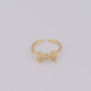 May include: A gold ring featuring a bow design, embellished with tiny clear stones.