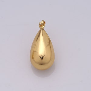 May include: A gold-colored teardrop pendant with a smooth, reflective surface. The pendant has a small loop at the top for a chain. The teardrop shape is rounded and symmetrical, reflecting light.