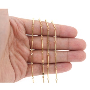 Puede incluir: Cinco cadenas de oro con un diseño de eslabón de barra. Las cadenas están dispuestas en una fila en una mano, con la cadena más corta en la parte superior y la cadena más larga en la parte inferior.