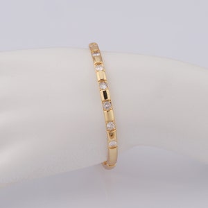 Puede incluir: Un brazalete de oro con una fila de piedras redondas transparentes.