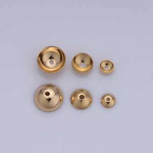 Op de afbeelding: Zes gouden metalen kralencapsules in verschillende maten. De capsules zijn rond en hebben een klein gaatje in het midden.