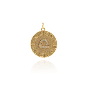 May include: Gold zodiac pendant featuring the Libra symbol with clear crystals. The pendant is surrounded by a circle of zodiac signs.