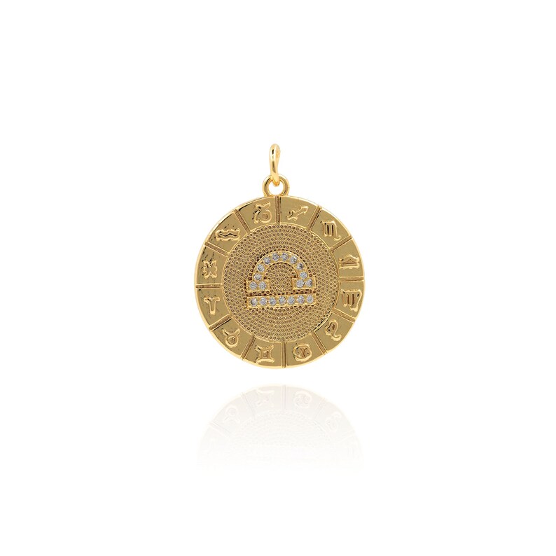 May include: Gold zodiac pendant featuring the Libra symbol with clear crystals. The pendant is surrounded by a circle of zodiac signs.