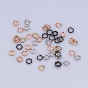 Peut inclure: Assortiment de petits anneaux de saut en métal de couleur argent, or et noir. Les anneaux de saut sont dispersés sur une surface blanche.