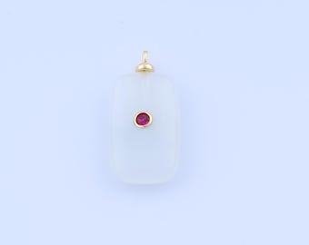 Puede incluir: Un colgante rectangular con la parte superior redondeada y una pequeña gema roja redonda engastada en un bisel dorado. El colgante es de color pálido y opaco, y tiene una fianza dorada en la parte superior.