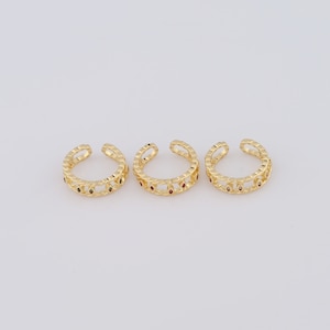 May include: Three gold ear cuffs with a delicate chain design and small red and green gemstones.