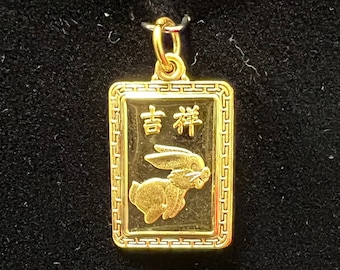 May include: A gold pendant with a rectangular frame and a detailed design. The pendant features a rabbit with the Chinese characters "吉利" (pronounced "jī lì") meaning "lucky" or "auspicious".