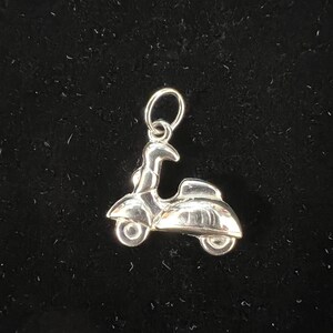 May include: Silver charm in the shape of a scooter. The charm has a loop at the top for attaching to a bracelet or necklace.