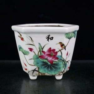 Peut inclure: Un pot hexagonal en céramique blanche avec un motif floral représentant des fleurs de lotus roses, des feuilles vertes et deux petits oiseaux. Le pot a trois petits pieds et le mot "和" est peint sur le devant.