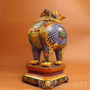 Puede incluir: Un quemador de incienso cloisonné con forma de criatura mítica con un patrón de escamas azul, verde y dorado. La criatura se alza sobre una base rectangular decorada con motivos rojos, naranjas y florales. El texto goodhappy5077 es visible abajo.