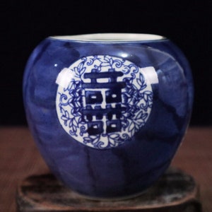 May include: A blue and white ceramic jar with a circular design featuring a Chinese character and floral motifs. The jar has a glossy finish.