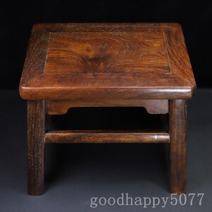May include: A small, square, dark brown wooden stool with a smooth, polished top surface showing natural wood grain patterns. The stool features four straight legs connected by horizontal support bars on each side and the text goodhappy5077.