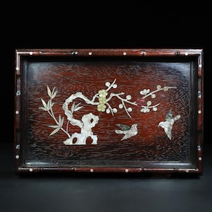 May include: A rectangular wooden tray with a dark reddish-brown finish. The tray is decorated with inlaid mother-of-pearl and features a branch with flowers and two birds. The frame has a bamboo-like design with white accents.