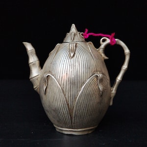 May include: A silver teapot with a bamboo handle and a lotus flower design. The teapot has a textured surface and a lid with a finial.