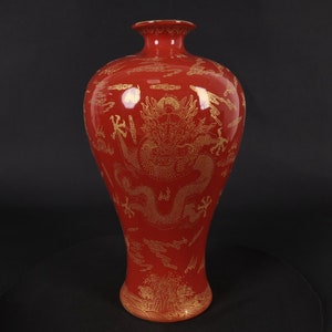 Op de afbeelding: Een rode keramische vaas met een gouden drakenontwerp. De vaas heeft een brede basis en een smalle hals.