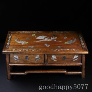 May include: A rectangular wooden table with two drawers, featuring intricate mother-of-pearl inlay designs of fish, lotus flowers, and leaves on the top surface and drawer fronts, set against a dark brown wood grain finish with small metal pulls.