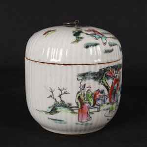 Può includere: Vaso in porcellana bianca con coperchio e manico argentato. Il vaso è decorato con una scena colorata di persone in un giardino con alberi e fiori.