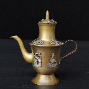 Könnte beinhalten: Eine Messing-Teekanne mit Deckel und Ausguss. Die Teekanne ist mit geprägten Drachen und anderen Designs verziert. Die Teekanne steht auf einem schwarzen Hintergrund.