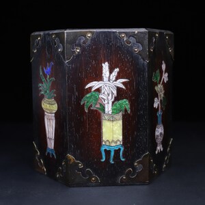 May include: A hexagonal dark wood brush pot featuring inlaid mother-of-pearl and colored stone floral designs on each panel. The corners are reinforced with brass metal plates secured by small rivets, creating a structured and decorative container.