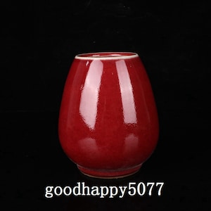 Może przedstawiać: Czerwony ceramiczny wazon o zaokrąglonym, bulwiastym kształcie. Wazon ma gładkie, błyszczące wykończenie.