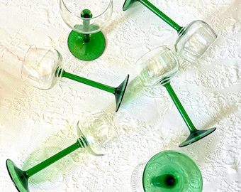 May include: Set of six green stemmed wine glasses with clear glass bowls. The glasses are arranged on a white lace tablecloth.