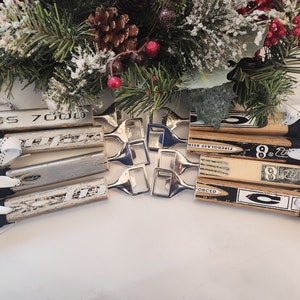Peut inclure: Six ouvre-bouteilles en forme de bâton de hockey en bois avec des logos et des numéros d'équipe en noir et blanc. Les ouvre-bouteilles sont attachés avec des lacets de hockey blancs et noirs. Les ouvre-bouteilles sont disposés en forme d'étoile avec cinq ouvre-bouteilles argentés au centre.