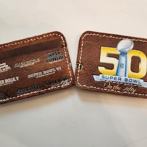 Może przedstawiać: Dwa brązowe skórzane etui na karty. Jeden ma logo Super Bowl 50 z napisem "On the fifty". Drugi wyświetla logo i tekst Super Bowl z poprzednich gier. Oba mają białe szwy.