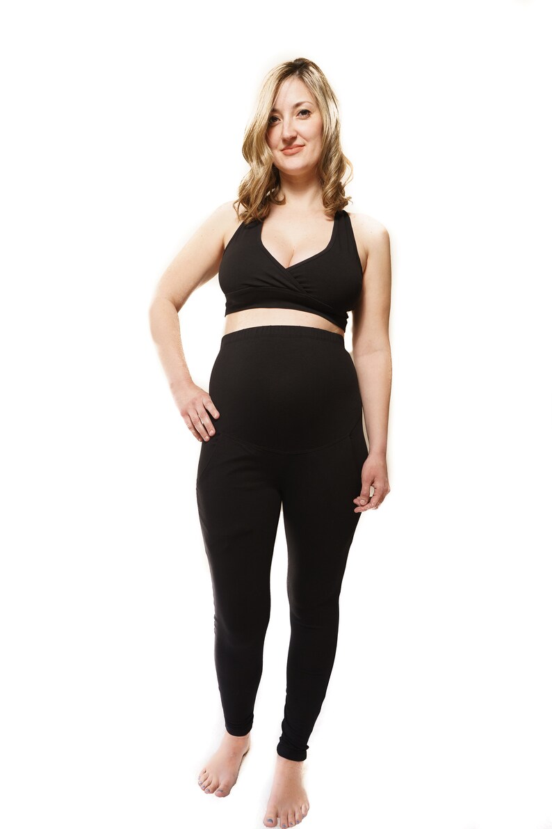 Puede incluir: Una persona embarazada con un top de maternidad negro y leggings negros. El top tiene un dise&ntilde;o de envoltura y los leggings tienen una cintura alta.