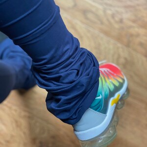 May include: A pair of blue leggings with the bottom portion bunched up, showing the white, green, yellow, orange, and red of a rainbow-colored sneaker.