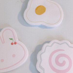 May include: A collection of three pastel-colored, die-cut stickers. One is shaped like a fried egg with a yellow yolk, another is a pink bunny with cherries, and the third is a narutomaki design.
