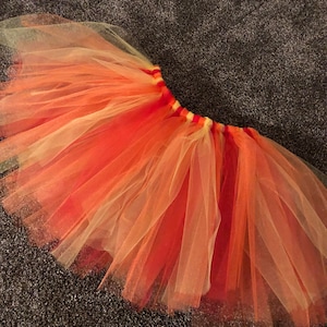 May include: A multi-layered tulle skirt in shades of orange, yellow, and white. The skirt is gathered at the waist and has a soft, flowing silhouette.