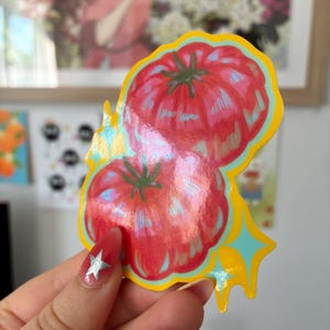 K&ouml;nnte beinhalten: Ein farbenfroher Aufkleber mit zwei roten Tomaten mit gr&uuml;nen Stielen. Der Aufkleber hat einen gelben Rand mit blauen und gelben Sternen-Akzenten. Die Tomaten haben ein gl&auml;nzendes, schillerndes Finish.