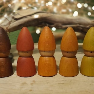 Puede incluir: Cinco figuritas de gnomos de madera con caras y sombreros pintados. Los gnomos están pintados en tonos de marrón, naranja, amarillo y verde.